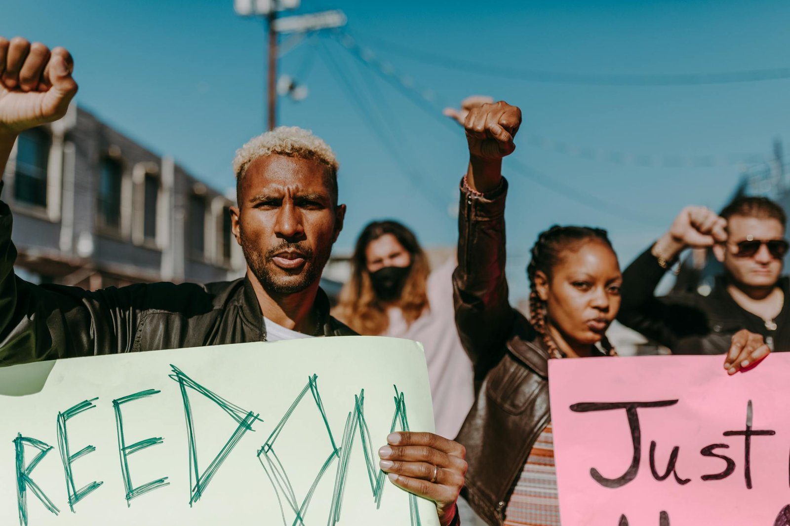 A diverse crowd of adults protesting outdoors, holding signs and raising fists for freedom and justice.